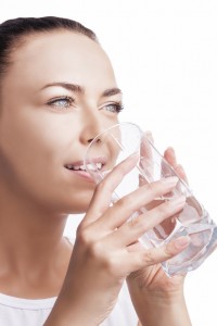 Health Concept: Portrait of Happy Smiling Caucasian Brunette Woman Drinking Clear Water from Glass. Isolated Over Pure White Background. Vertical Image